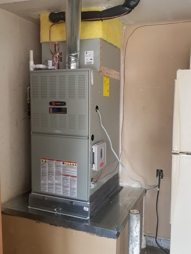 A Trane furnace installed on a sheet-metal base in a garage closet