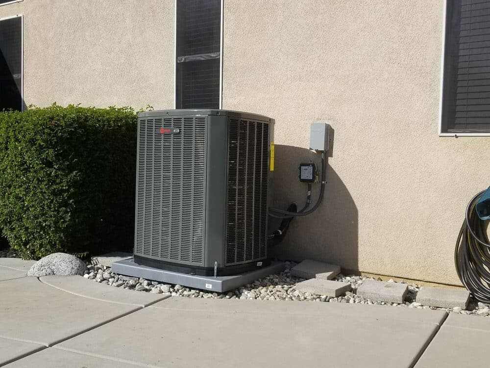 A condenser installed at the corner of a house with the disconnect box above it