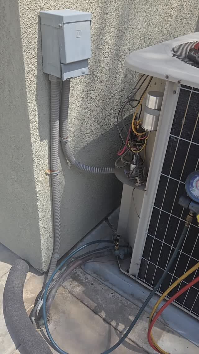 A condenser with the service panel open, wiring exposed, and gauge hoses connected