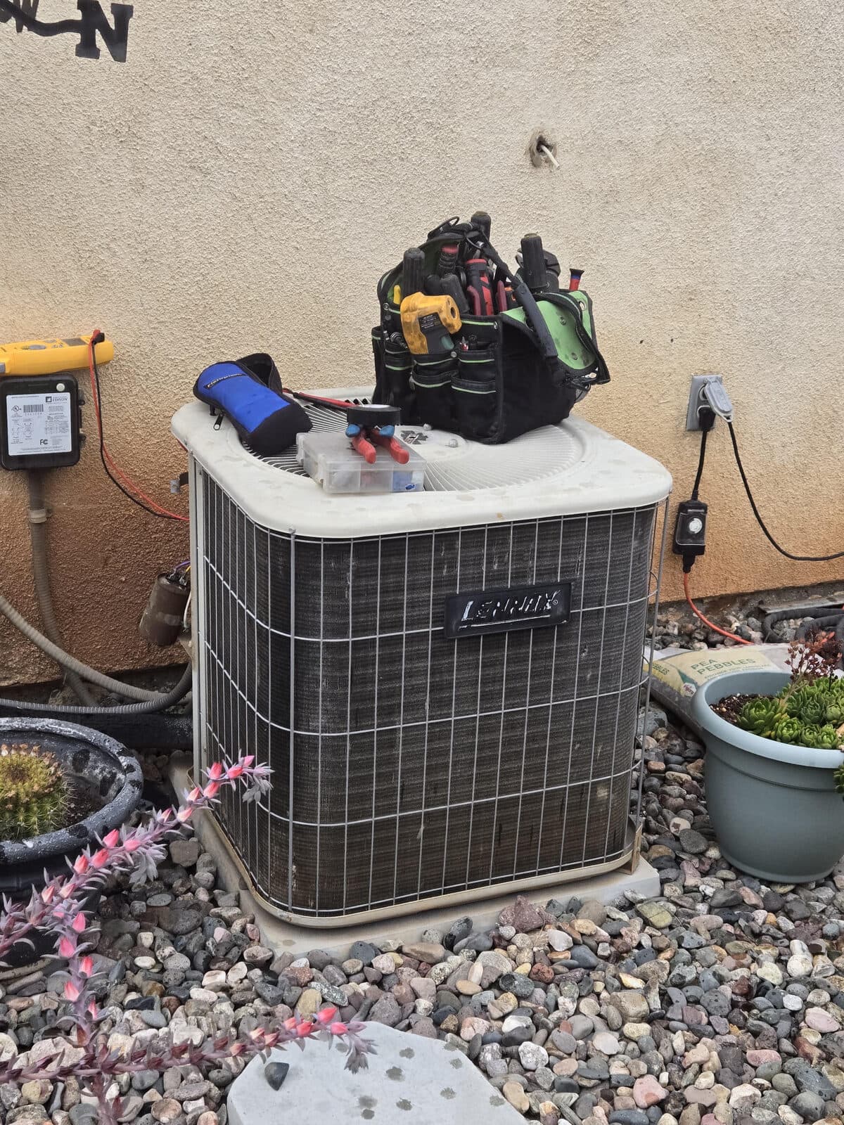 A condenser with a tech's tool bag, capacitor tester, and multimeter laid out on top