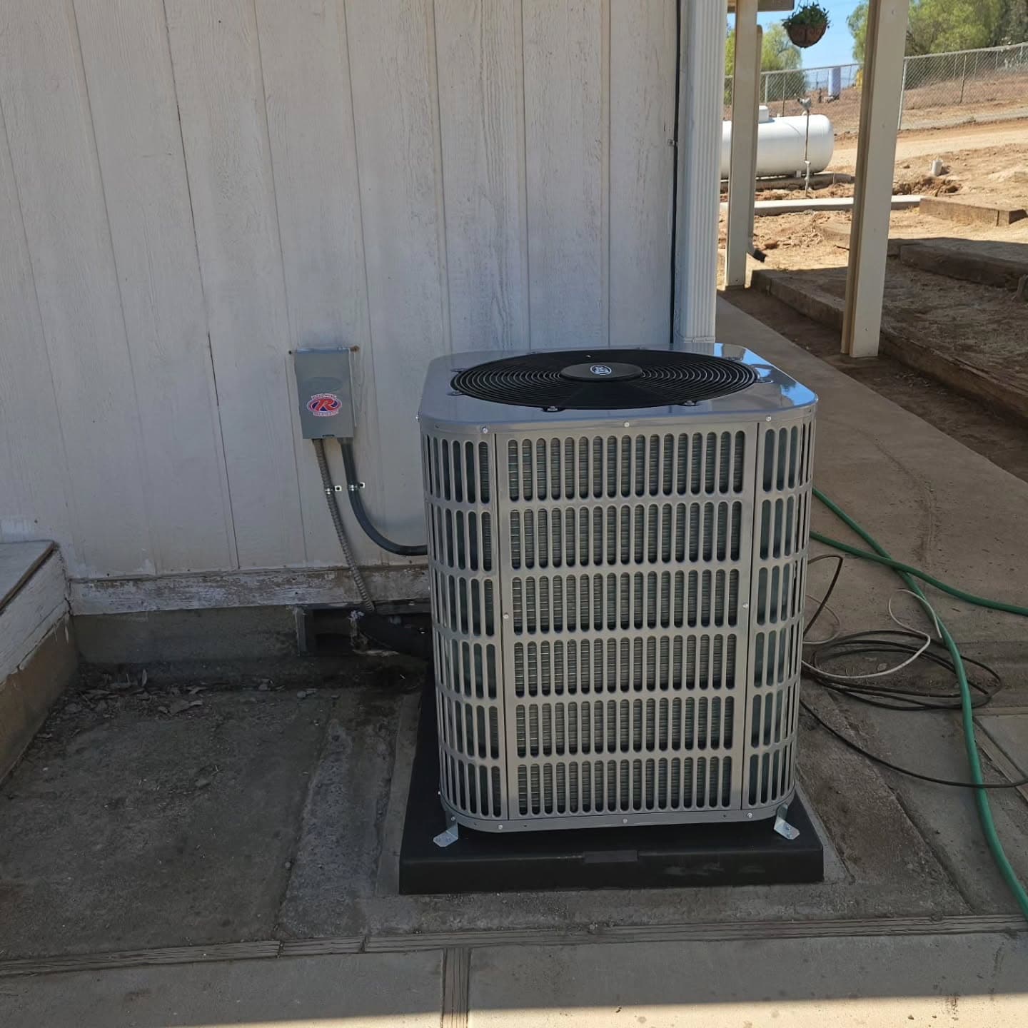 A condenser set on a pad beside a manufactured home's skirting