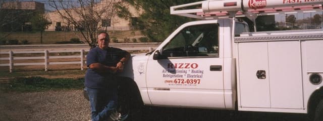 A Rizzo owner beside a white service truck lettered RIZZO — Air Conditioning, Heating, Refrigeration, Electrical