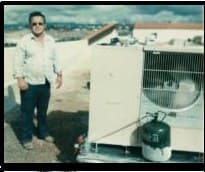 An early Rizzo technician in sunglasses standing on a rooftop beside a vintage packaged air-conditioning unit