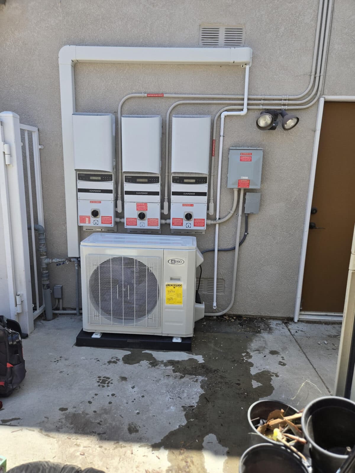 A mini-split condenser mounted below a row of solar inverters on a stucco wall