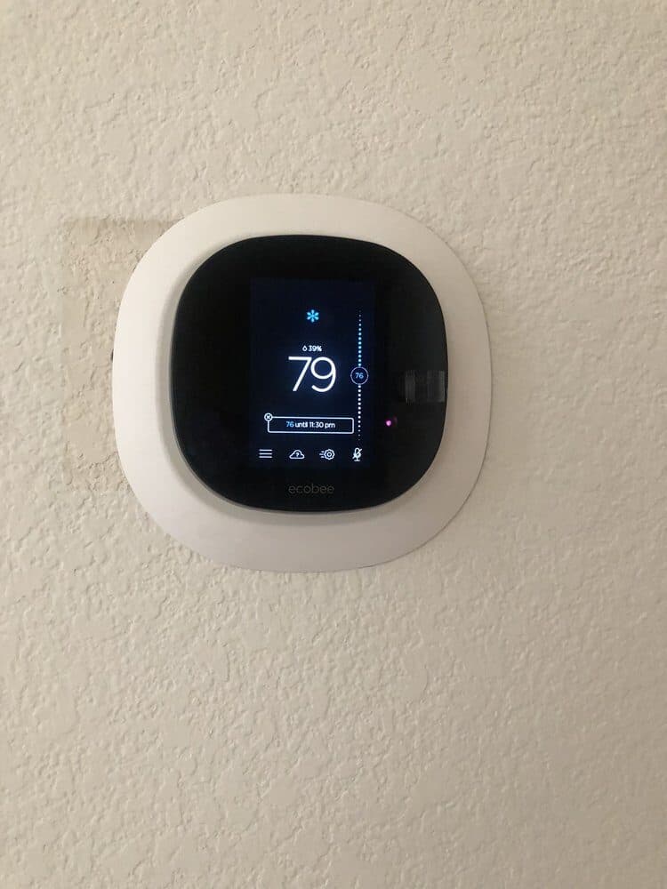 An ecobee smart thermostat mounted on a painted interior wall, its screen showing the target temperature and schedule