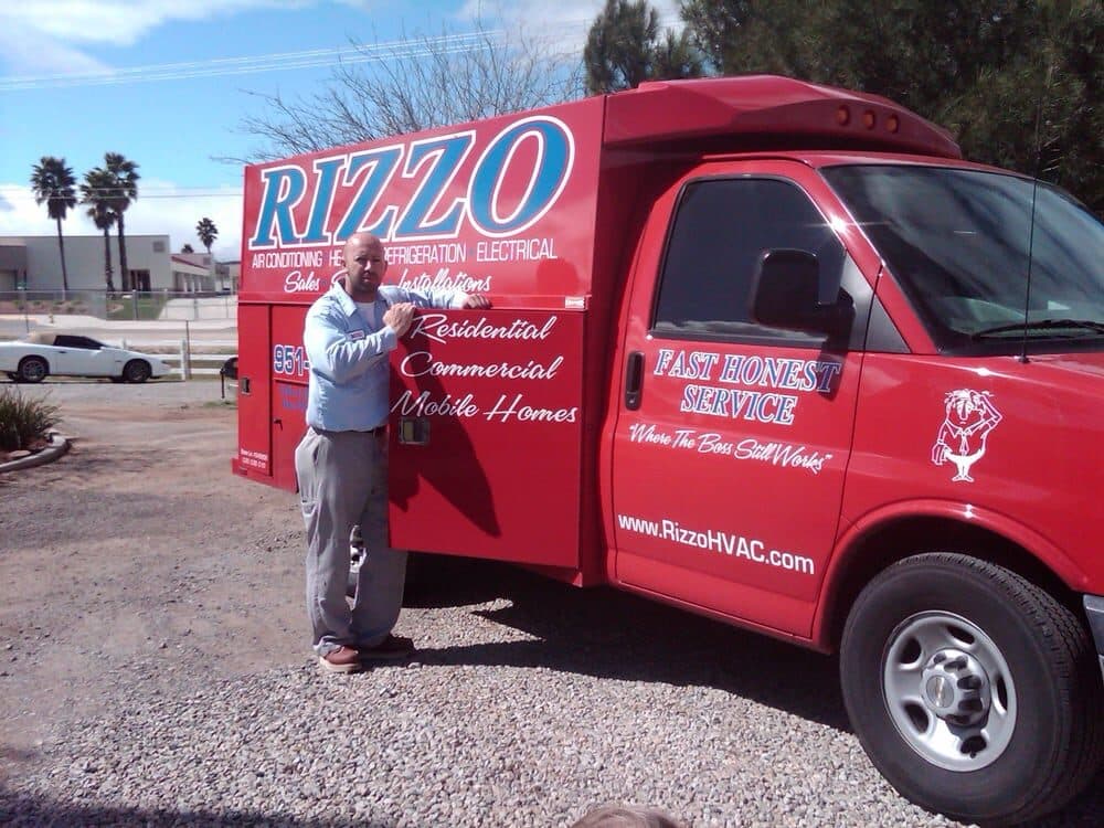 The present-day fleet of red Rizzo trucks and vans parked outside the company shop beneath the RIZZO Heating & A/C sign