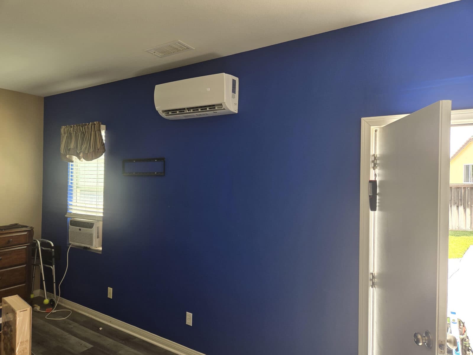 A finished ductless mini-split head mounted high on a blue bedroom wall