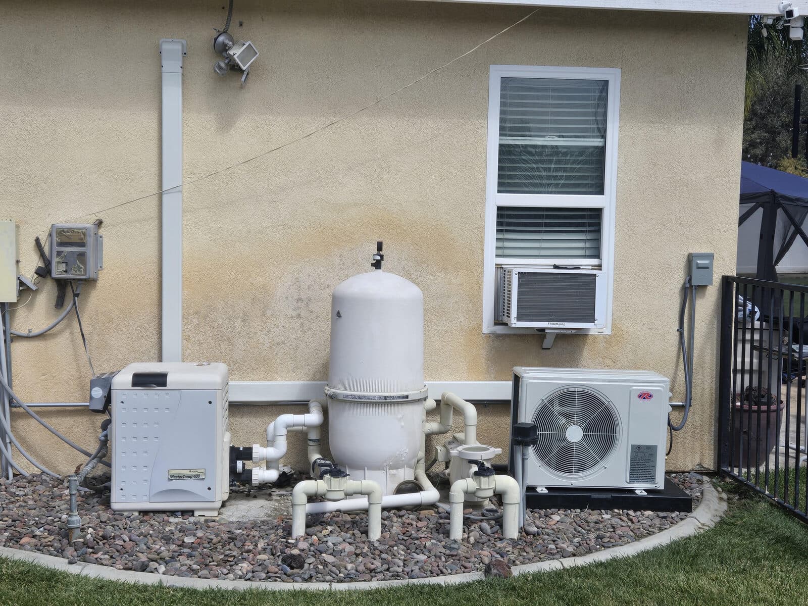 A white mini-split condenser installed beside pool equipment against a stucco wall