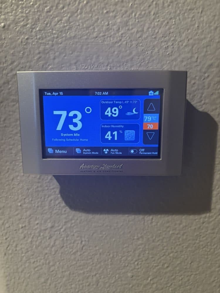 An American Standard touchscreen thermostat installed level on a wall