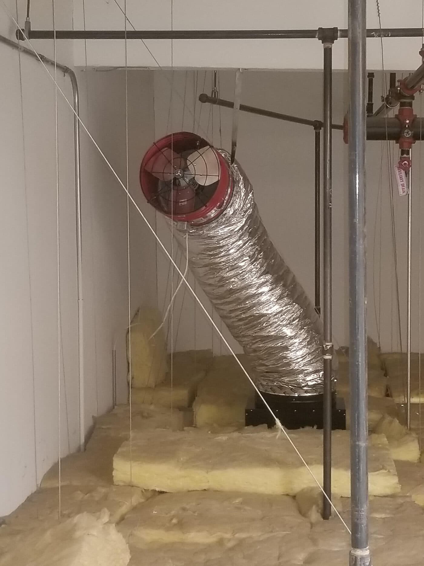 A red ducted whole-house fan hung above the ceiling with insulated flex duct running down to the ceiling damper box