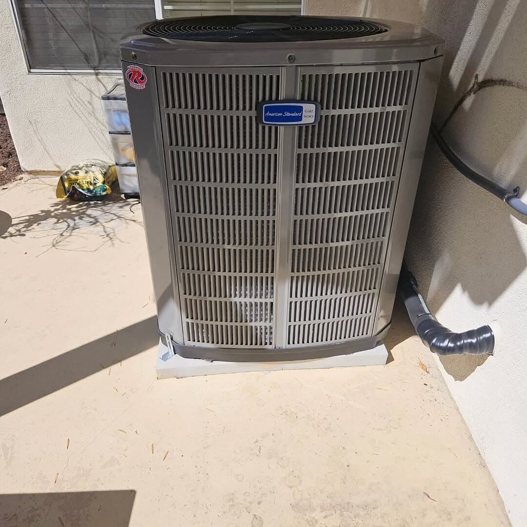The replacement American Standard condenser set on a new pad against the same wall