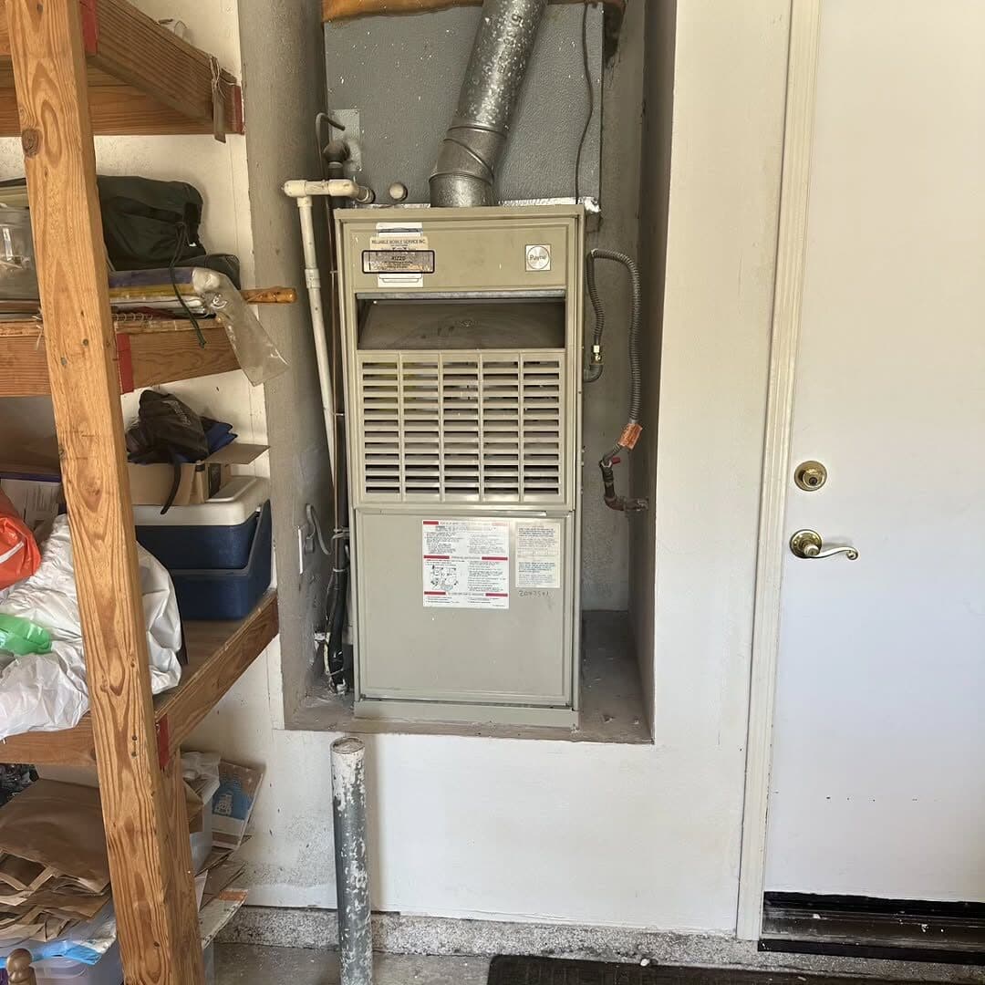 The old beige furnace in a garage closet with original ducting above it