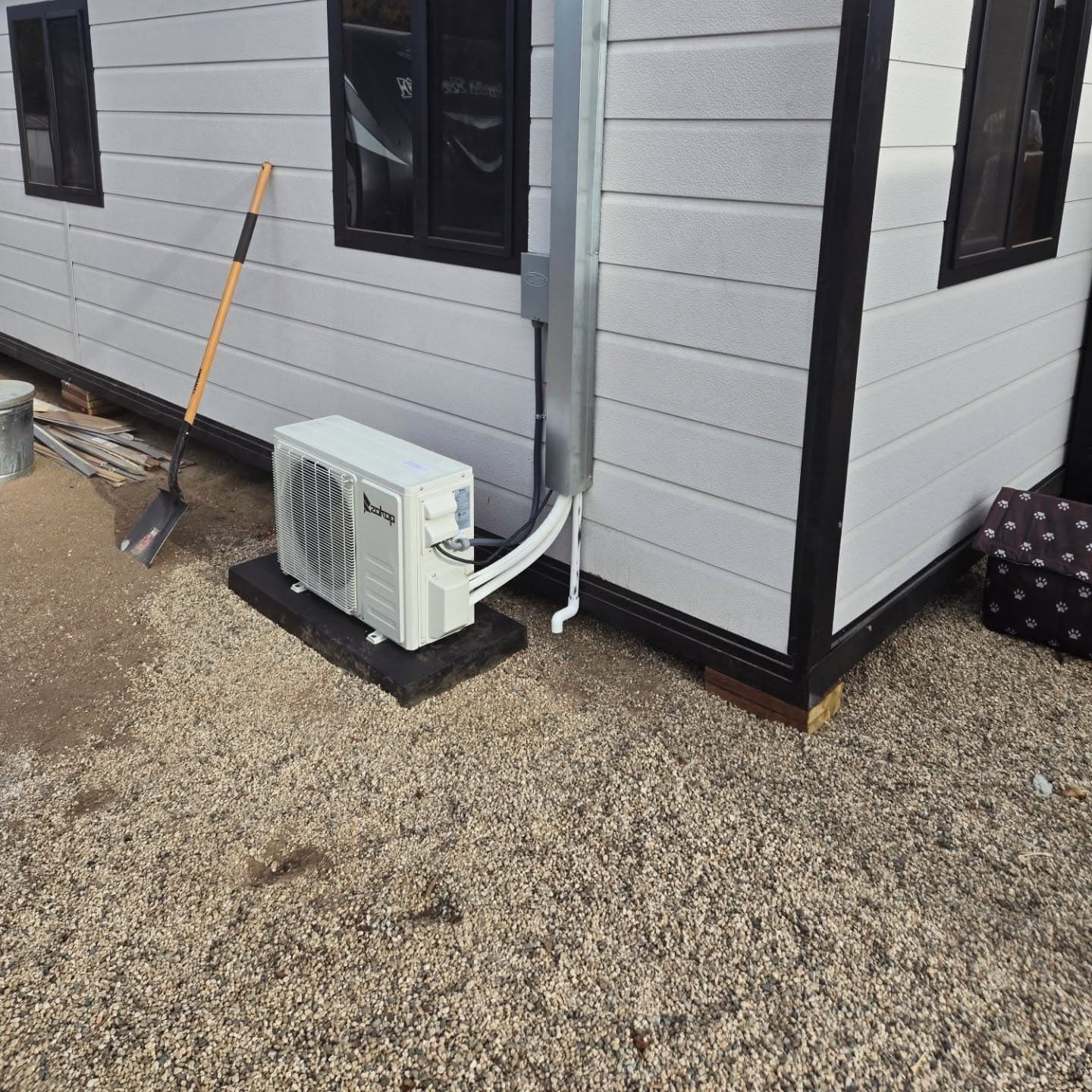 A Zokop mini-split outdoor unit on a pad at the skirting of the home, disconnect box above it and the line set run up a metal cover to the corner