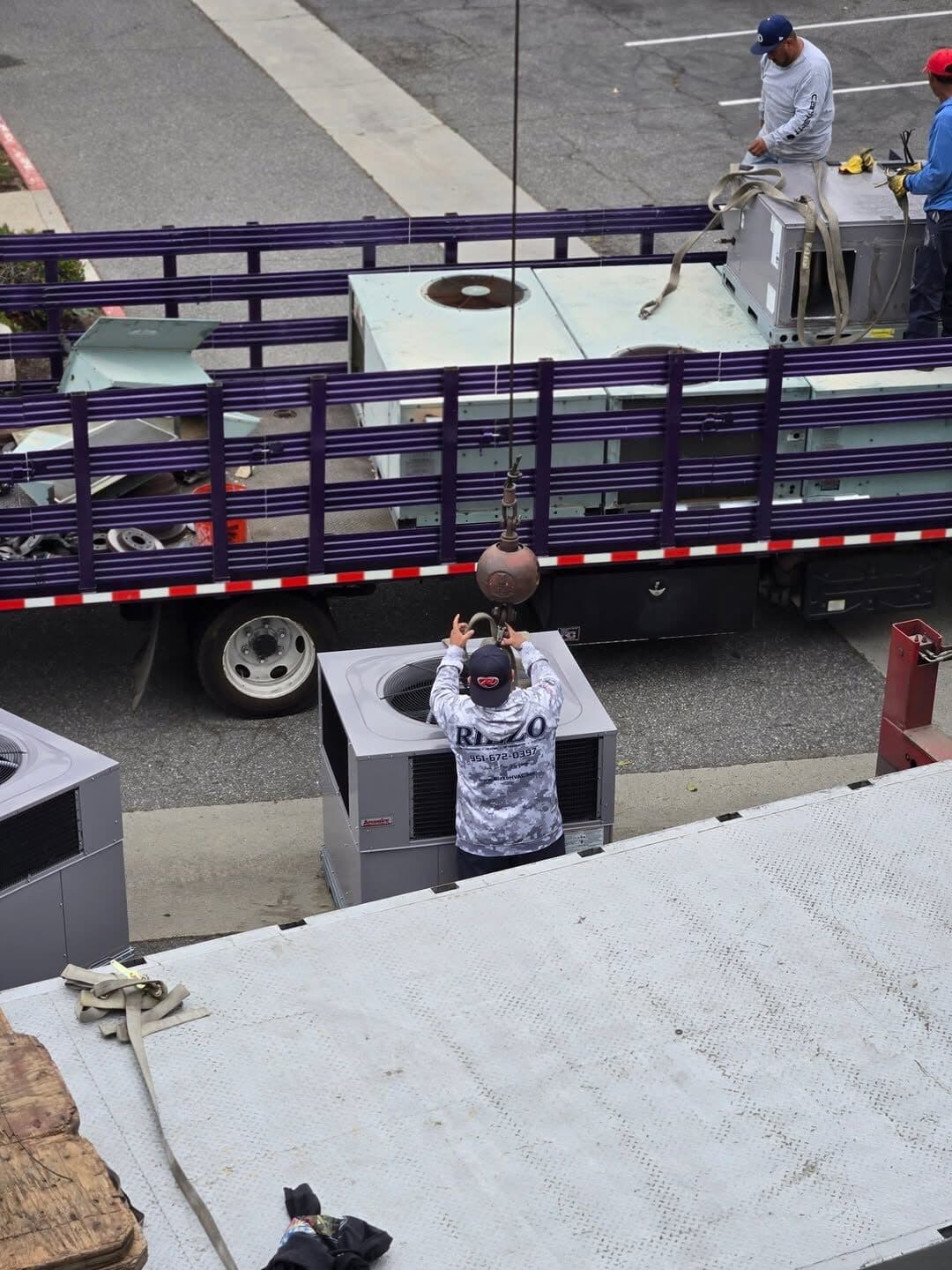 Crew loading the removed rooftop units onto a flatbed truck in the parking lot below